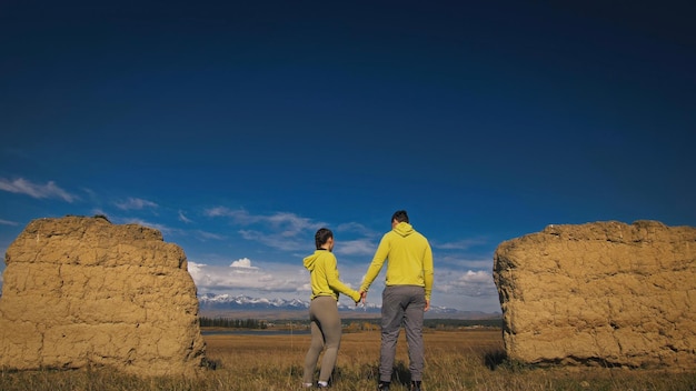 Homem e mulher em roupas esportivas verdes amarelas Lindo casal de viajantes abraçam e beijam perto de pedra velha apreciando a paisagem montanhosa