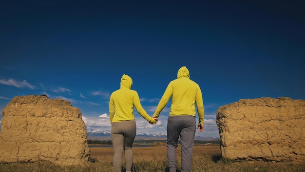 Homem e mulher em sportswear verde amarelo. lindo casal de viajantes abraçam e beijam perto de pedra velha, apreciando a paisagem das terras altas. dois viajantes estão caminhando contra o pano de fundo das montanhas cobertas de neve.