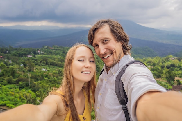 Homem e mulher fazendo selfie no fundo do vulcão Batur e vista para a montanha Agung na manhã de Kintamani Bali Indonésia