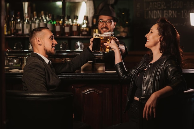 Homem e mulher felizes tilintam copos de cerveja com o barman no balcão do bar