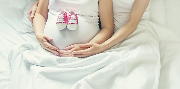 Homem e mulher grávida abraçam a barriga e seguram sapatos de bebê. foco seletivo.