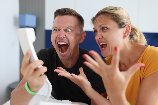 Homem e mulher gritando no receptor do telefone em um quarto de hotel