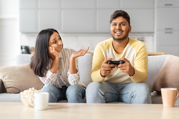 Homem e mulher indianos a jogar videogame no sofá.