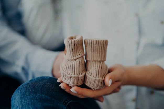 Homem e mulher irreconhecíveis antecipam para o bebê segura sapatinhos pequenos. Conceito de paternidade de maternidade familiar. Futuros pais. Aniversário