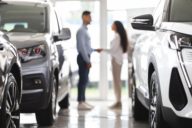 Homem e mulher irreconhecíveis apertando as mãos no showroom de automóveis