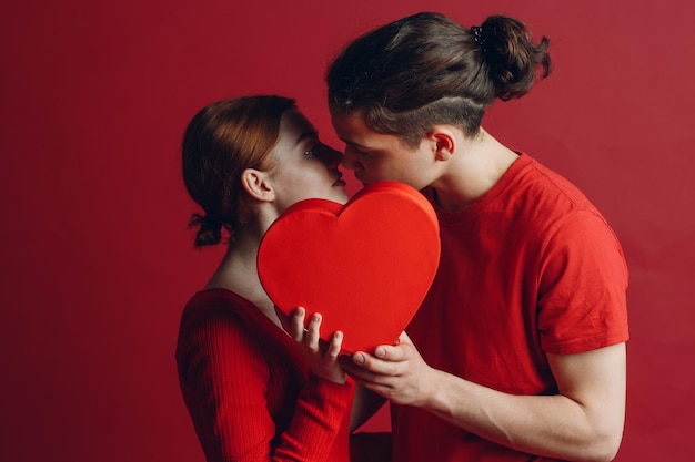 Homem e mulher jovem casal beijando e se escondendo atrás de uma caixa em forma de coração