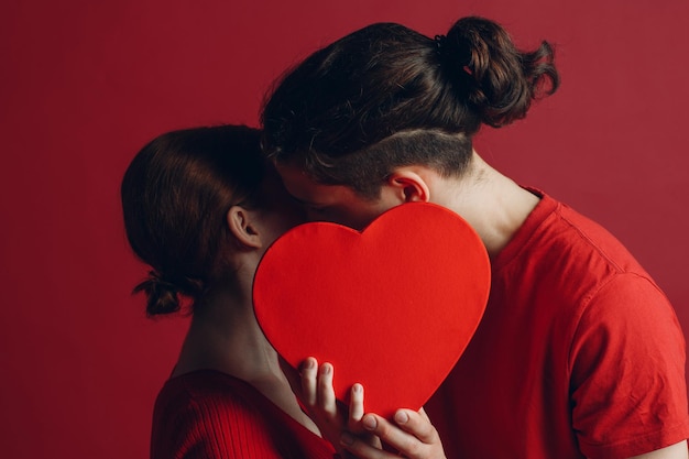 Homem e mulher jovem casal beijando e se escondendo atrás de uma caixa em forma de coração