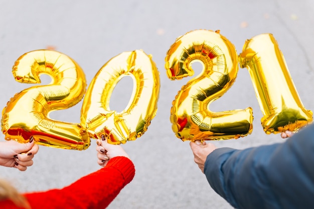 Homem e mulher par de mãos segurando o numeral 2021 dos balões da folha de ouro. Conceito de celebração do ano novo.