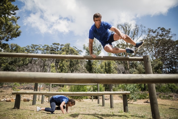 Homem e mulher pulando obstáculos durante a pista de obstáculos no campo de treinamento