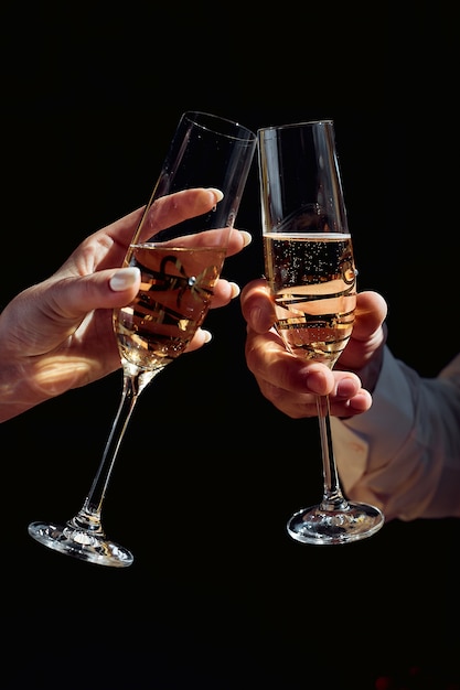 homem e mulher queixo queixo com taças de champanhe, mão feminina e masculina segura um copo com champanhe no escuro