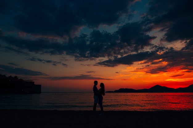 Homem e mulher se abraçando na praia ao pôr do sol.