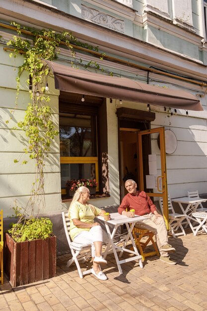 Homem e mulher sênior alegres com xícaras de café sentados em um café de rua