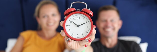 Homem e mulher sorridentes deitados na cama e segurando o despertador às dez horas da rotina de sono em