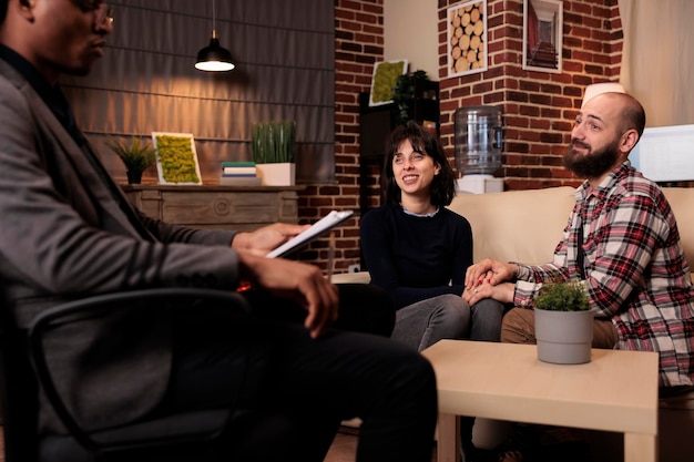 Homem e mulher sorrindo depois de resolver problemas de relacionamento, sentindo-se felizes com a reconciliação e de mãos dadas. Recebendo ajuda de aconselhamento e aconselhamento na sessão de terapia com especialista masculino.