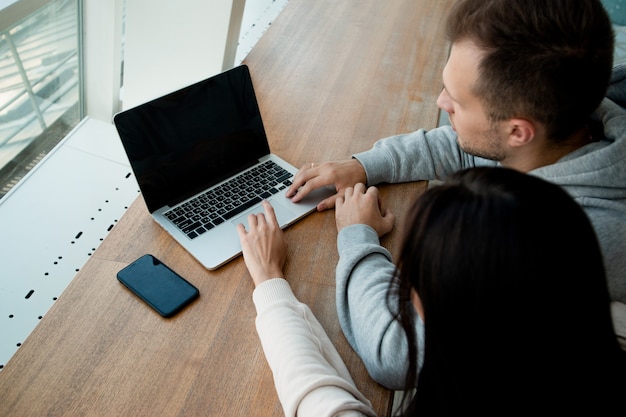 Homem e mulher trabalham juntos no laptop. colegas sentam-se em um café para trabalhar em um projeto comum. conceito de coworking. café em segundo plano. laptop cinza moderno.