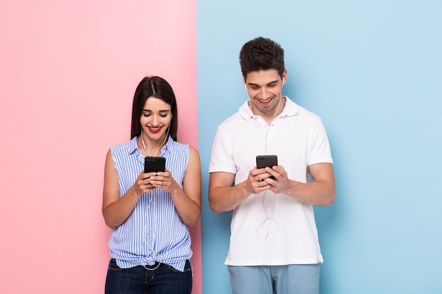 Homem e mulher usando fones de ouvido e smartphones, isolados sobre uma parede colorida