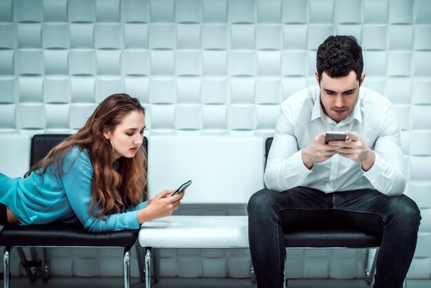 Foto homem e mulher usando o telefone enquanto estão sentados em uma cadeira contra a parede