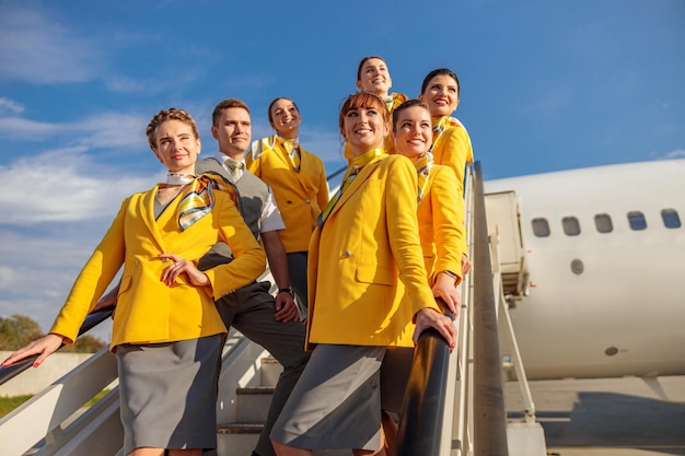 Homem e mulheres sorridentes comissários de bordo em uniforme de aviação em pé nas escadas de embarque de avião