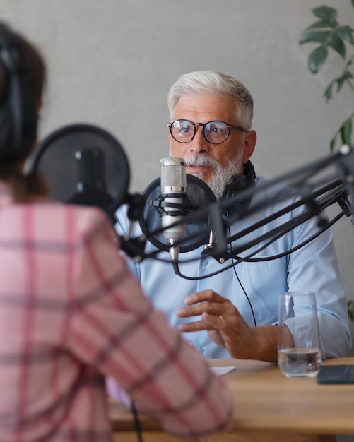 Homem e uma mulher gravam um podcast ou entrevista com um microfone em um estúdio de gravação adulto