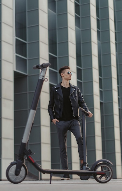 Homem elegante atraente em óculos de sol está posando para o fotógrafo com duas scooters.