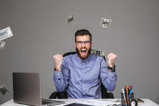 Homem elegante barbudo gritando alegre em óculos se alegra sentado à mesa no escritório