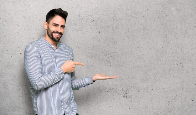 Homem elegante com camisa segurando copyspace imaginário na palma da mão para inserir um anúncio sobre parede texturizada