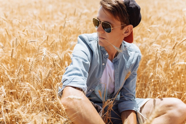 Homem elegante com óculos de sol no campo de trigo