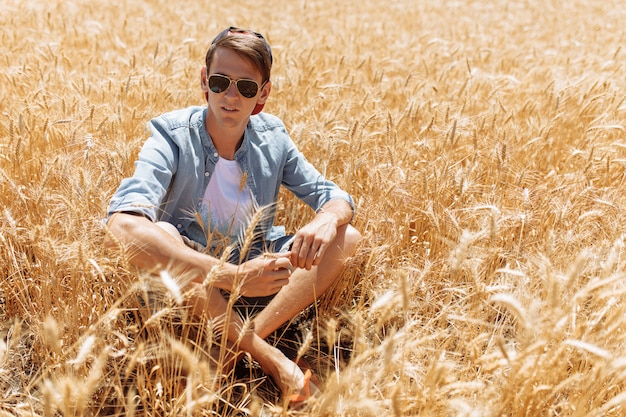 Homem elegante com óculos de sol no campo de trigo