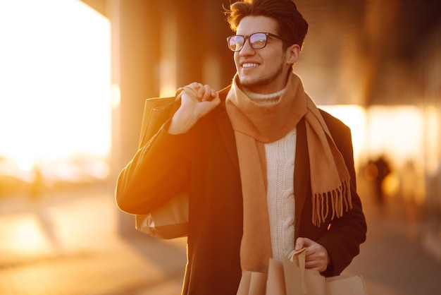 Homem elegante com pacotes de papel depois de fazer compras ao pôr do sol Homem bonito fazendo compras