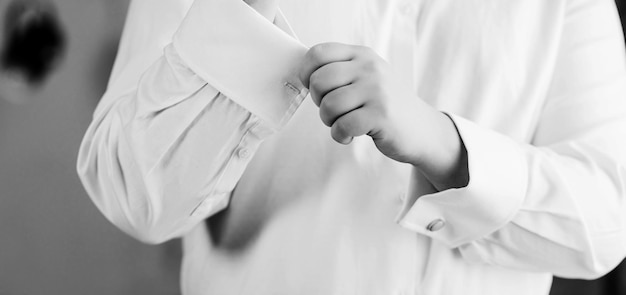 Homem elegante de camisa branca está abotoando joias de abotoaduras