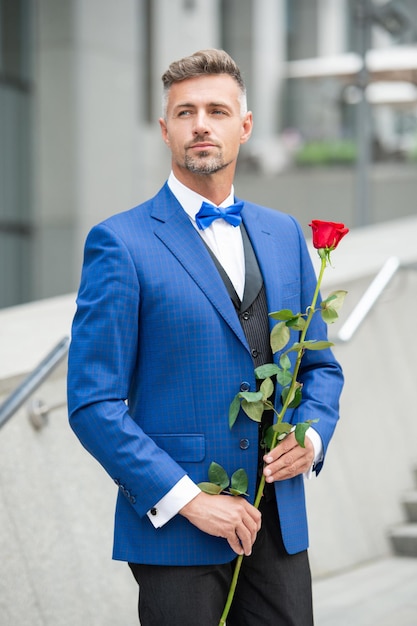 Homem elegante de smoking homem usar gravata borboleta de smoking ao ar livre homem de smoking bonito com rosa vermelha