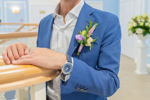 Homem elegante de ternoBoutonniere de eremurus branco eustoma e vegetação preso ao noivo jaqueta azul Detalhes do casamento e florística