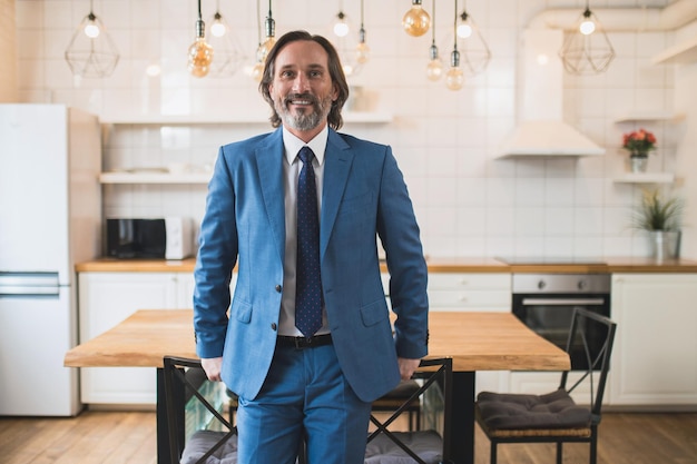 Homem elegante e bonito de terno azul em pé perto da mesa na sala