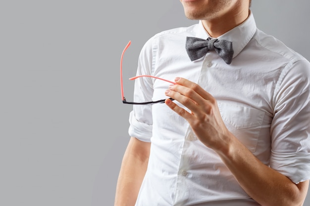 Homem elegante e moderno em uma camisa branca com uma gravata borboleta segurando copos na mão.