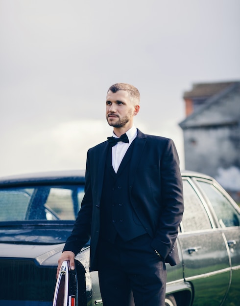 Homem elegante em uma fantasia perto de um carro velho