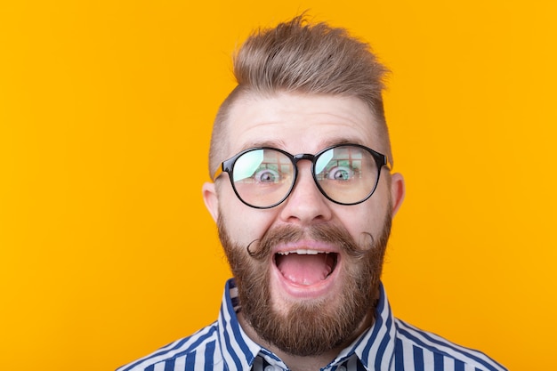 Homem elegante jovem hippie com bigode e barba abre a boca com alegria em uma parede amarela. Conceito de surpresa e celebração. Copyspace.