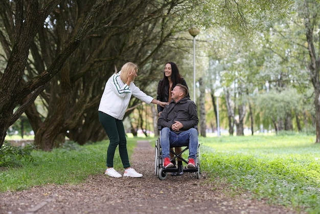 Homem em cadeira de rodas e amigas rindo caminhando no parque para reabilitação de pessoas com deficiência