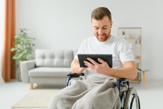 Homem em cadeira de rodas usando computador tablet em casa Homem aposentado positivo com deficiência física navegando na web no touch pad assistindo vídeo on-line em ambientes fechados