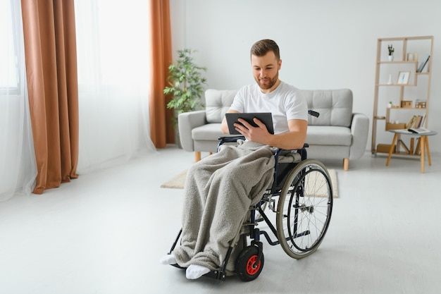 Homem em cadeira de rodas usando computador tablet em casa Homem aposentado positivo com deficiência física navegando na web no touch pad assistindo vídeo on-line em ambientes fechados