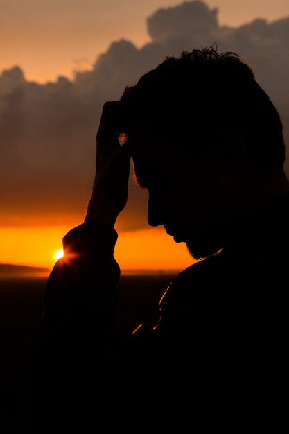 Homem em campo no pôr do sol. Silhueta de jovem na natureza