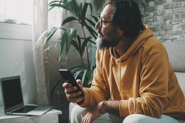 Homem em casa em conexão de tecnologia lazer atividade moderna usar telefone celular e laptop Um povo do sexo masculino pensando e olhando para fora da janela interna Problemas e procurando a vida do conceito de ideia