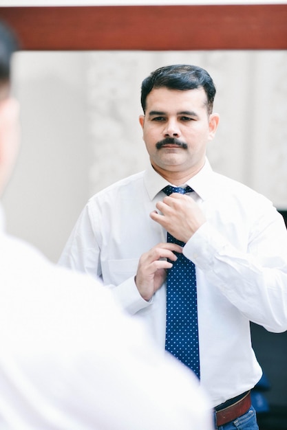 homem em frente ao espelho, usar camisa branca e gravata modelo indiano do Paquistão