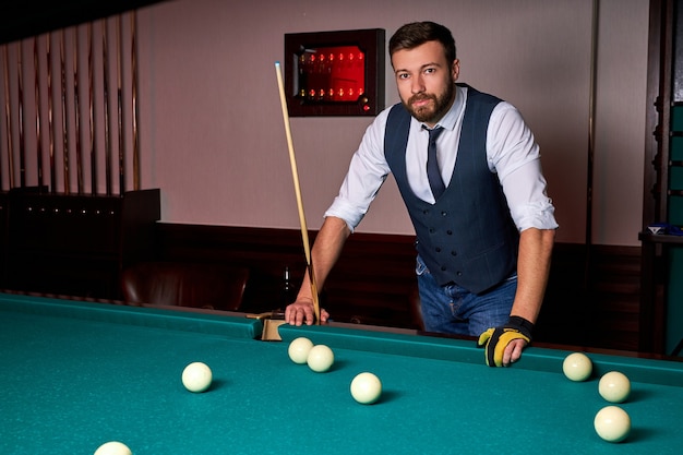 Homem em pé ao lado da mesa de bilhar, posando, com roupa formal. retrato