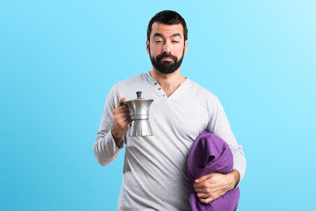 Homem em pijama segurando uma cafeteira em fundo colorido