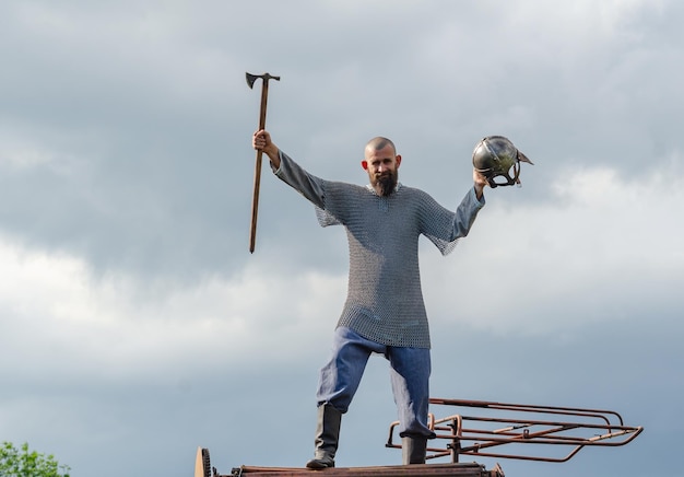 Foto homem em roupas medievais armadura viking capacete de metal e machado de cadeia na mão fundo de cinza escuro céu nublado pessoa