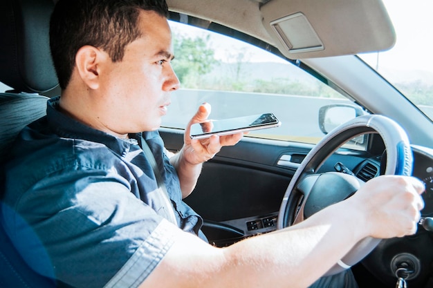 Homem em seu carro enviando notas de voz com seu celular Vista lateral de um homem em carro usando telefone