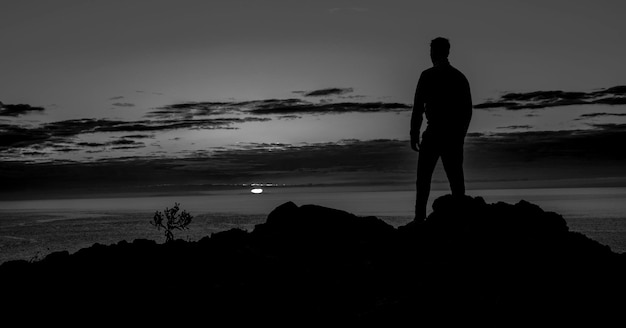 Foto homem em silhueta de pé em uma rocha na praia contra o céu