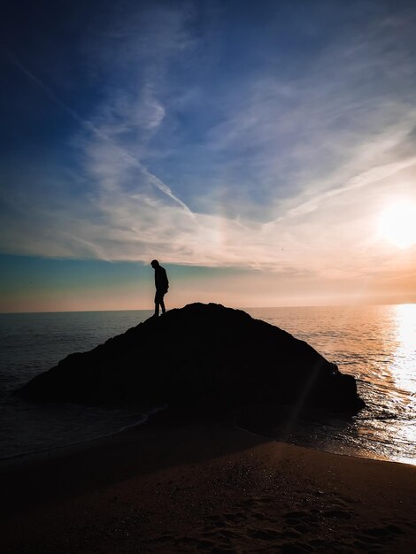 Foto homem em silhueta de pé na praia contra o céu durante o pôr do sol