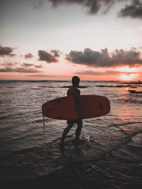 Foto homem em silhueta de pé na praia contra o céu durante o pôr do sol