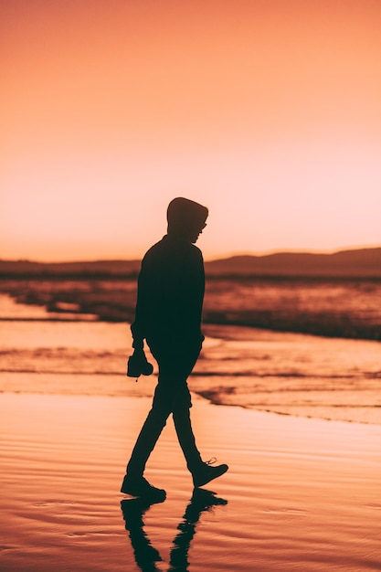 Foto homem em silhueta de pé na praia contra o céu durante o pôr do sol